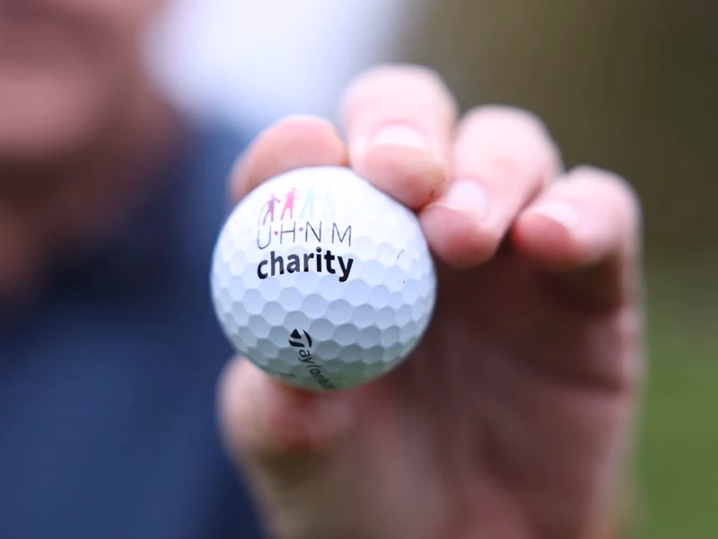 Close-up of a hand holding a UHNM Charity golf ball