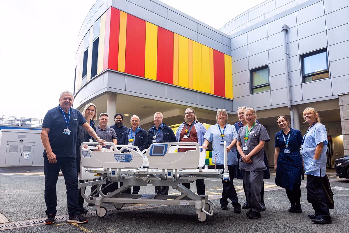 Hospital staff smiling gathered around a hospital bed outside the hospital building.