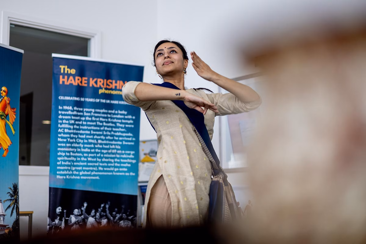 A woman dancing in front of a Hare Krishna Movement banner.