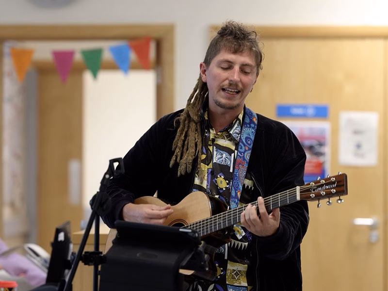Person playing an acoustic guitar in a hospital ward