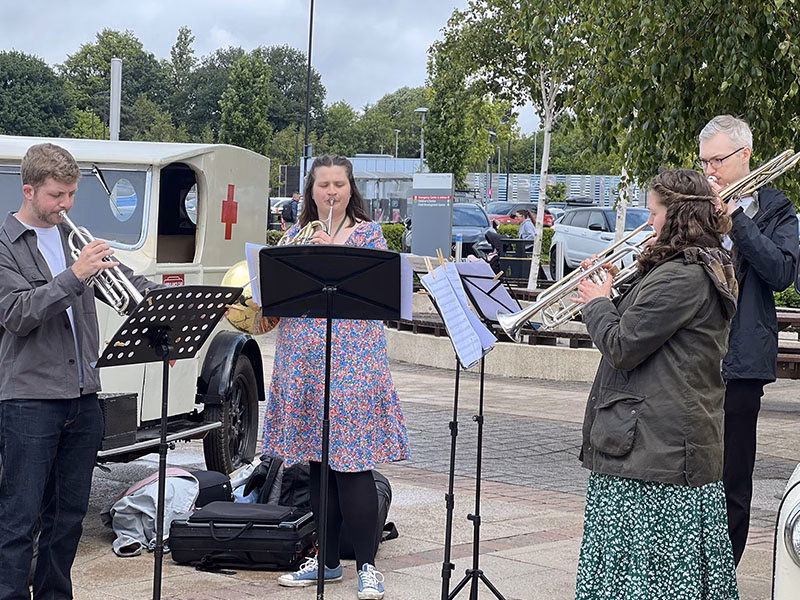 4 musicians playing wind instruments outside of a hospital