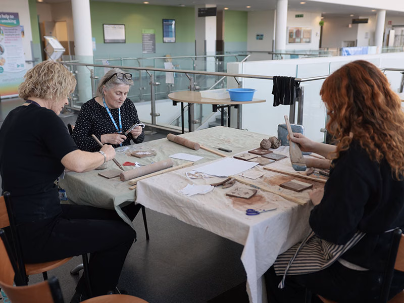 3 people sat around a table in a hospital painting ceramic tiles